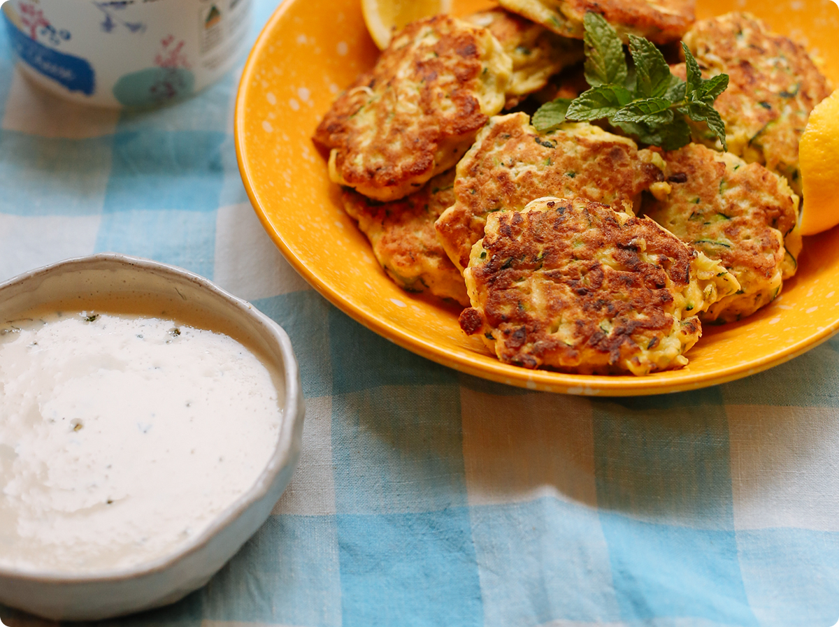 Golden-brown fritters served on a yellow plate with a sprig of mint, on a blue and white checkered tablecloth.